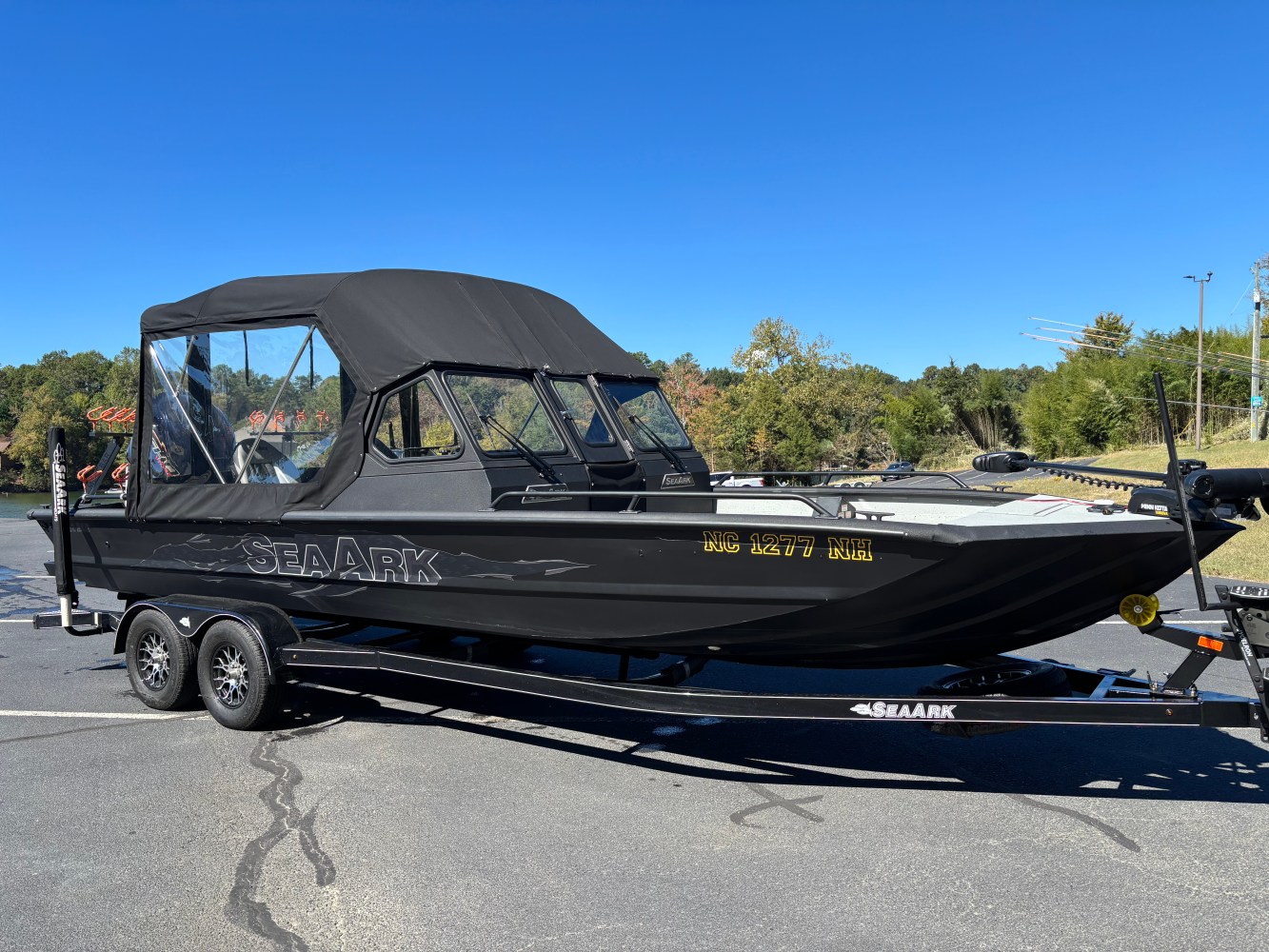 Black boat on a trailer in a parking lot with a canopy and clear windows.